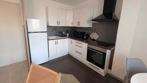 Una cocina compacta con armarios blancos, una estufa negra y un microondas.