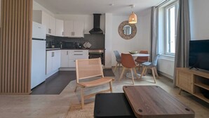 Un salón moderno con comedor, cocina y un televisor sobre un mueble de madera.