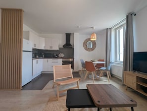 Ein modernes Wohnzimmer mit Essbereich, Küche und einem Fernseher auf einem Holzschrank.