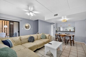 A living room with a beige sofa, a white coffee table, and a dining area with wooden chairs and a table.