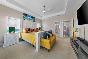 Um quarto com uma cama, um sofá amarelo, uma cômoda branca, uma televisão e um ventilador de teto.