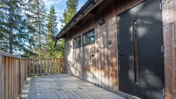 A wooden deck with a black garage door, surrounded by trees. - Gamla Wallesvägen 10 - Bruksvallarna (Bruksvallarna)