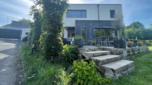 Un edificio moderno a due piani con una zona salotto esterna coperta e una scala in pietra che conduce all'ingresso.