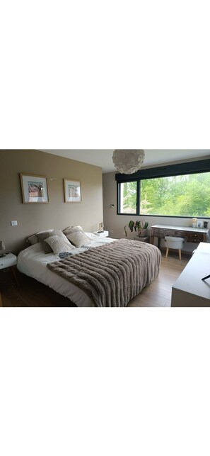 Ein Schlafzimmer mit Bett, Nachttischen, einem Schreibtisch und einem Fenster mit Blick auf Bäume.