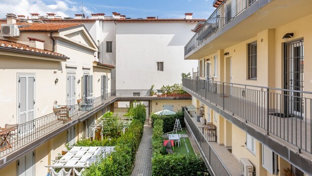 Un patio central con un sendero, rodeado de edificios con balcones y un pequeño jardín.
