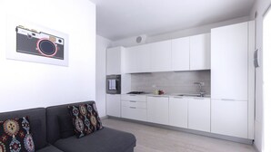Una cocina moderna con armarios blancos, horno empotrado y un sofá gris con cojines estampados.
