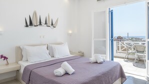 A bedroom with a bed, pillows, a bedside table with a vase, a wall-mounted light fixture, and a balcony with chairs. - Apartment in A Hotel 'Junior Suite Sea View B&B For 3 Guests' (Αγ. Γεώργιος)