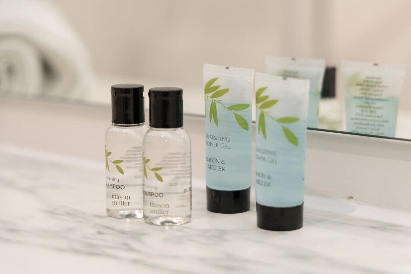 A bathroom counter with three bottles of Mason & Miller shampoo and two bottles of shower gel.