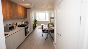 A modern kitchen with a microwave, stove, and dining area with a table set for two. - Sapphire Court Flat 69 2-Bedroom for family corporate or business travel (Birmingham)