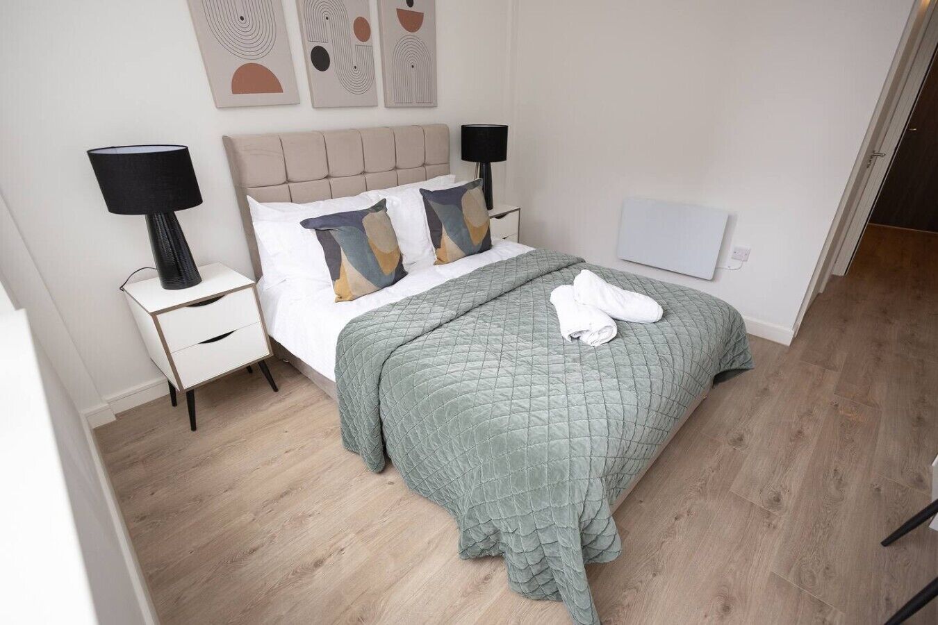 A neatly arranged bedroom with a bed, bedside tables, a lamp, and a quilted blanket.