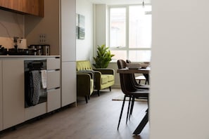 A modern kitchen with a dining area, a green sofa, and a large window. - Sapphire Court Flat 69 2-Bedroom for family corporate or business travel (Birmingham)