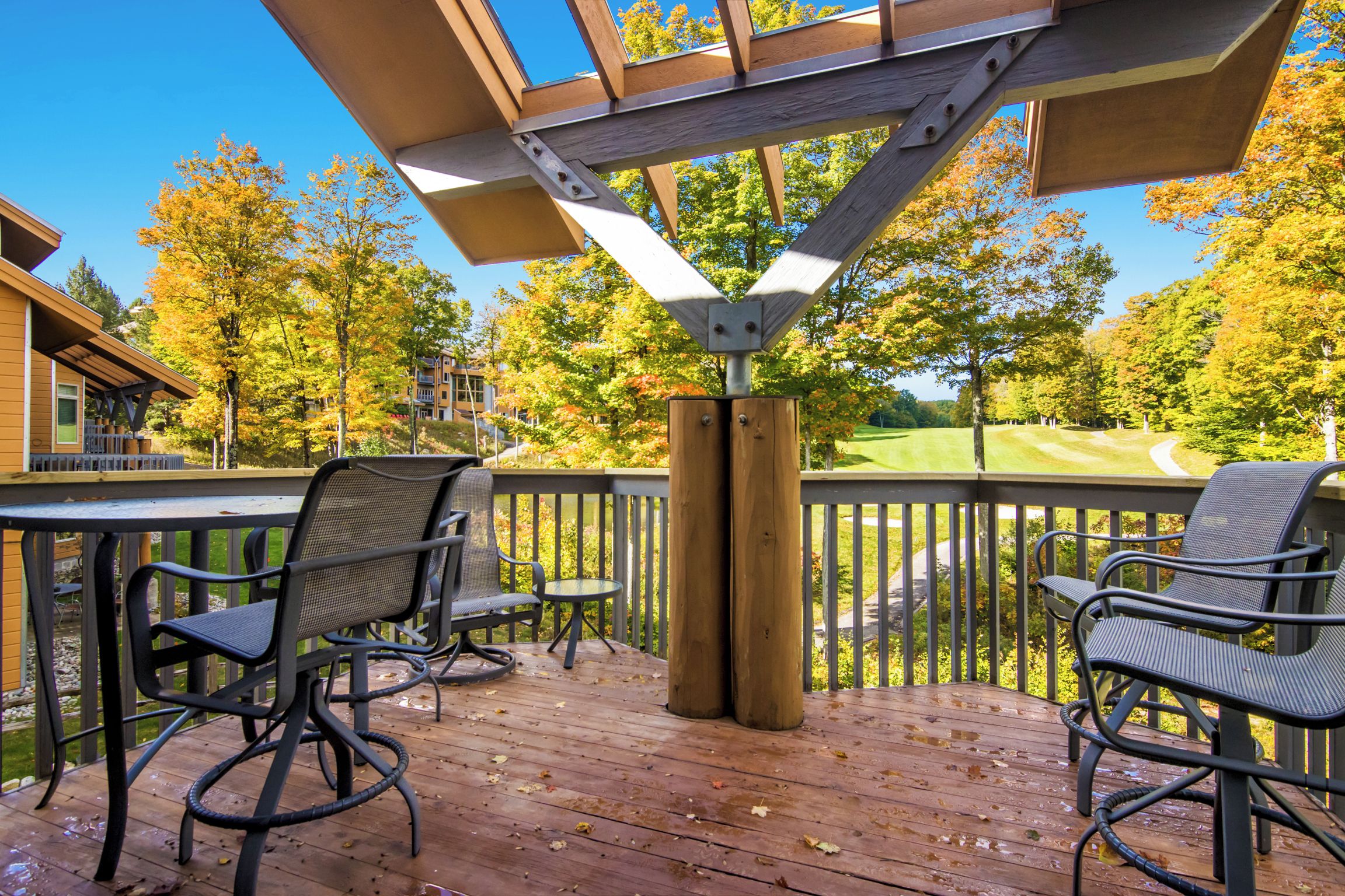 A wooden deck with metal chairs and a table, overlooking a golf course.