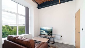 Ein modernes Wohnzimmer mit großem Fenster, einer Ledersofa, einem Fernseher auf einem Schrank und einem Holztisch.