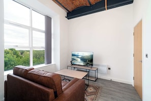 Ein modernes Wohnzimmer mit großem Fenster, einer Ledersofa, einem Fernseher auf einem Schrank und einem Holztisch.