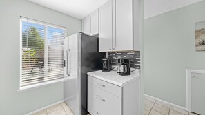 Eine moderne Küche mit Kühlschrank, Kaffeemaschine und einem Fenster mit Jalousien.