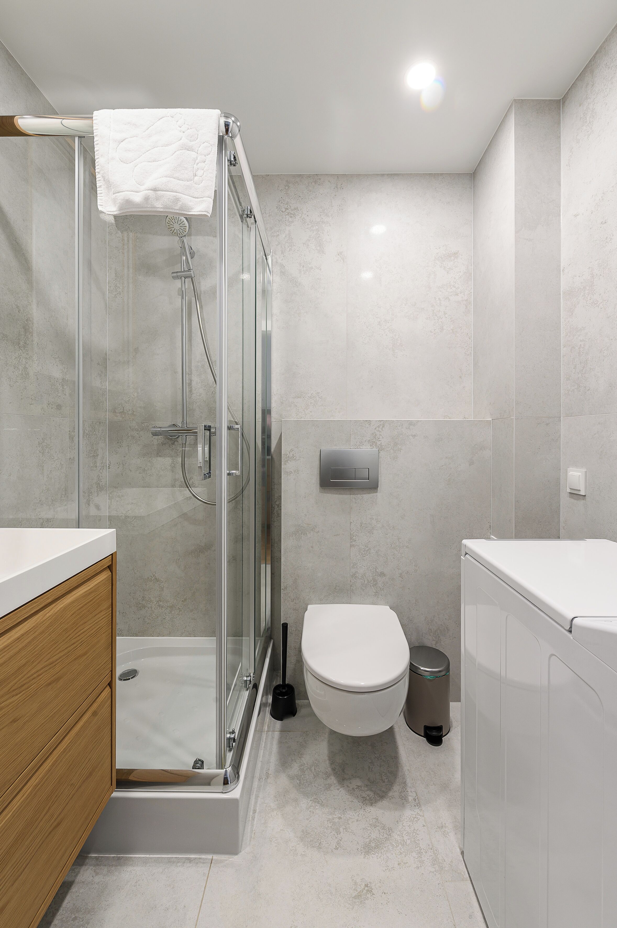 A modern bathroom with a glass-enclosed shower, a toilet, and a sink with a wooden cabinet.
