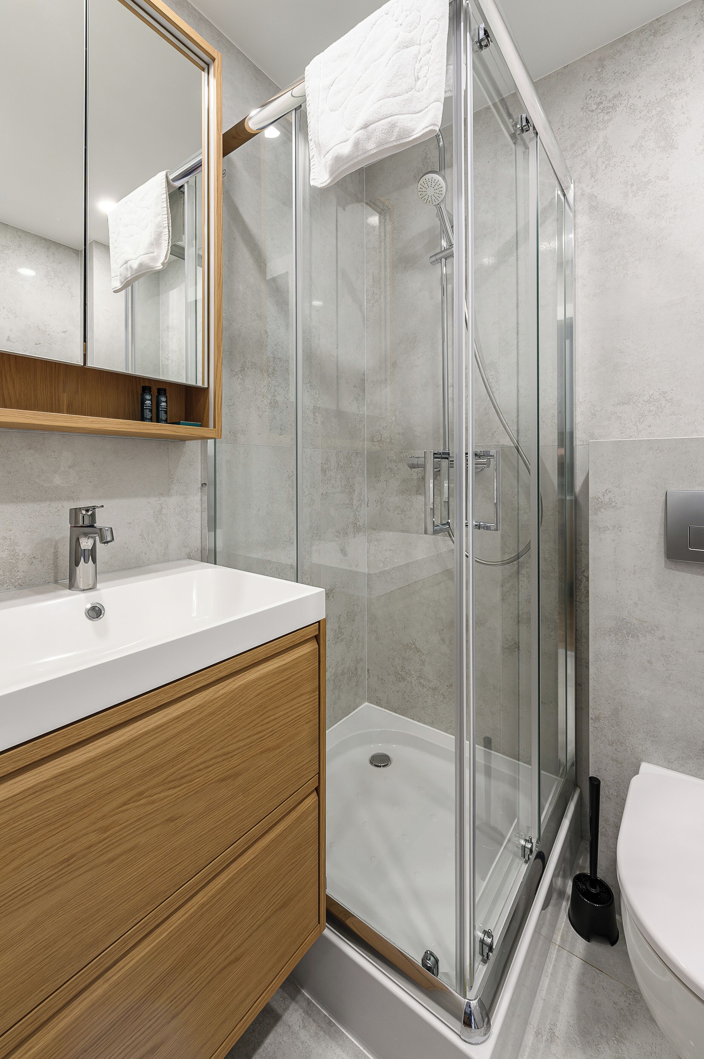 A modern bathroom with a glass-enclosed shower, a white sink, and a wooden vanity.
