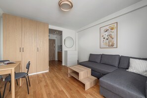 Ein modernes Wohnzimmer mit grauem Sofa, Holzboden, einem Esstisch mit Stühlen, einem Holzschrank und einem wandmontierten Spiegel.