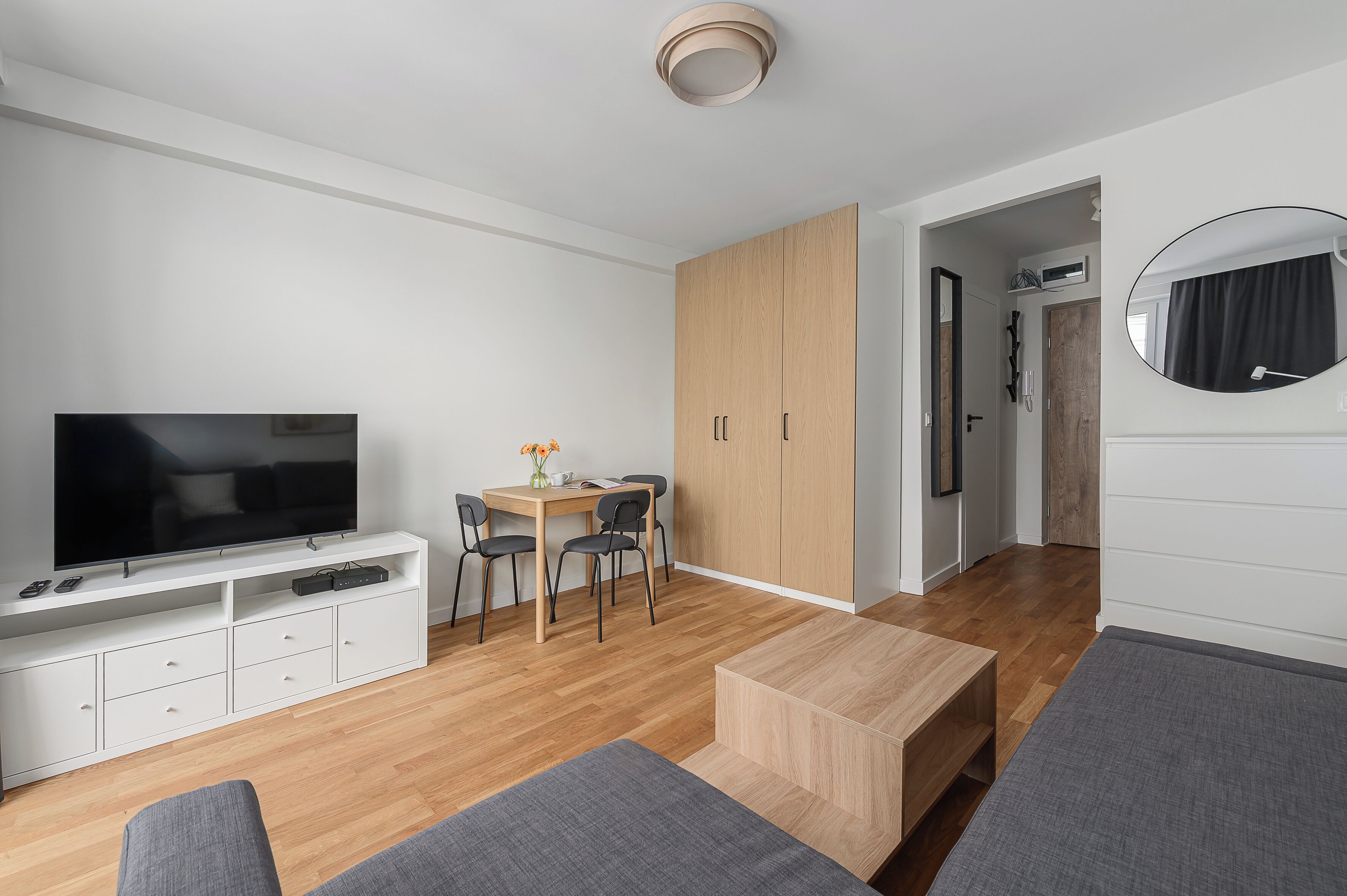Un soggiorno moderno con una TV a schermo piatto, un tavolo da pranzo in legno con sedie, un divano grigio e un ampio armadio.