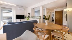 A modern living room with a sofa, a round wooden dining table, and a TV mounted on the wall. - Calming 1BR Apartment Acropolis view (Athens)