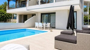 Et moderne hus med to etager, en swimmingpool, udendørs møbler og en balkon.