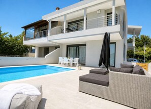 A modern two-story house with a swimming pool, outdoor seating, and a covered patio area.