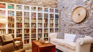 A cozy reading room with a stone wall, bookshelves, a leather armchair, a white sofa, and a wooden coffee table. - Bissantica, 17th-Century Stone House - Authentic Sardinia, Private Courtyard (Lunamatrona)