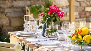 A table set outdoors with a stone wall backdrop, a hanging light fixture, and a vase with flowers. - Bissantica, 17th-Century Stone House - Authentic Sardinia, Private Courtyard (Lunamatrona)