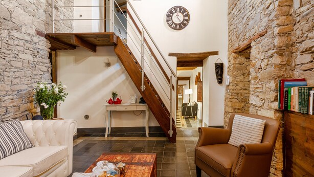 A spacious living area with a staircase, a clock, and a bookshelf. - Bissantica, 17th-Century Stone House - Authentic Sardinia, Private Courtyard (Lunamatrona)