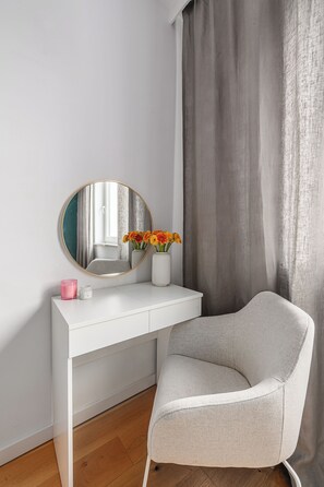 A white vanity with a round mirror, a vase with flowers, and a pink candle. - Lumina Apart nearManufartura and Parking (Łódź)