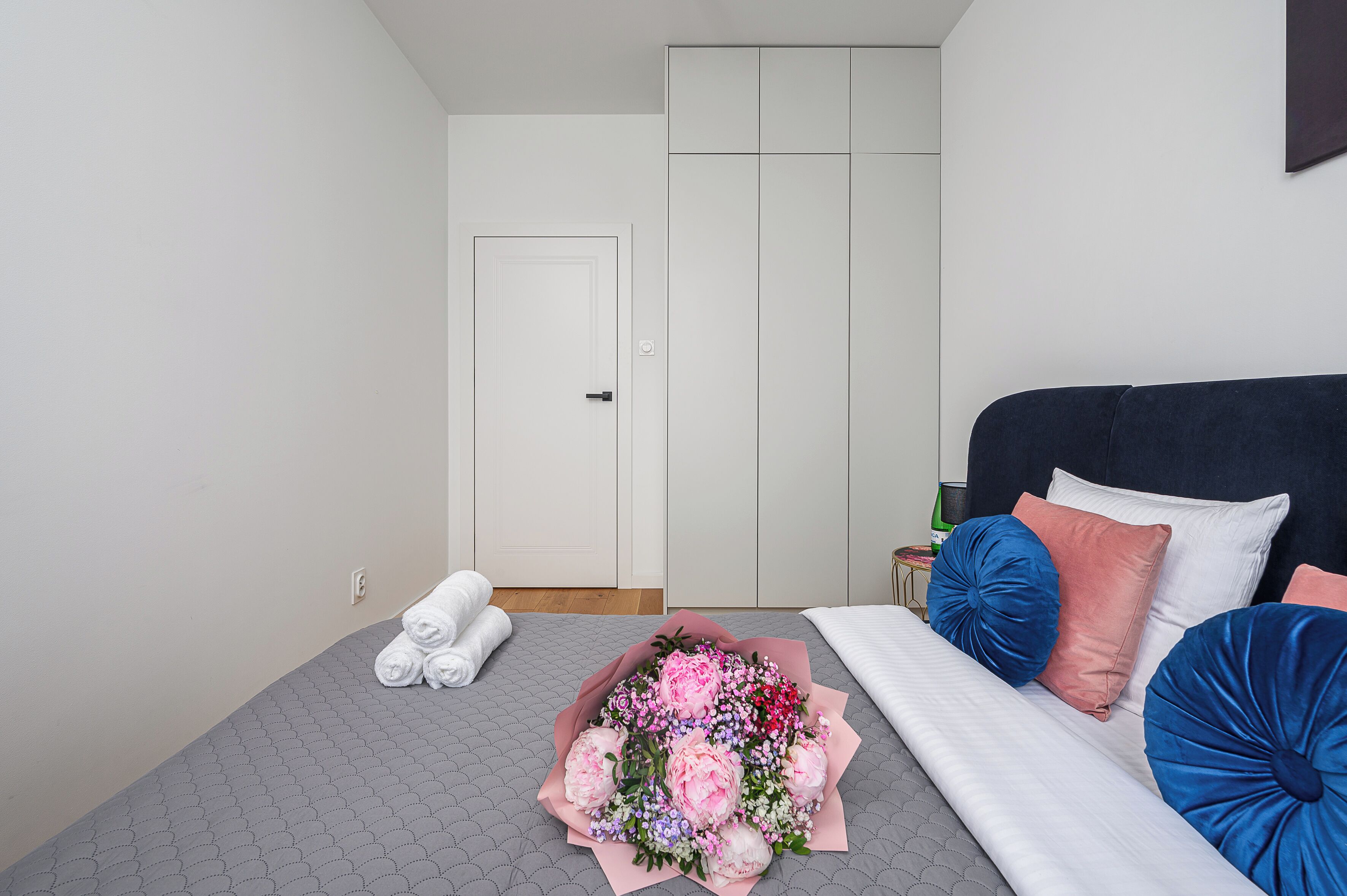 A neatly made bed with pillows, a bouquet of flowers, and a white door in a hotel room.