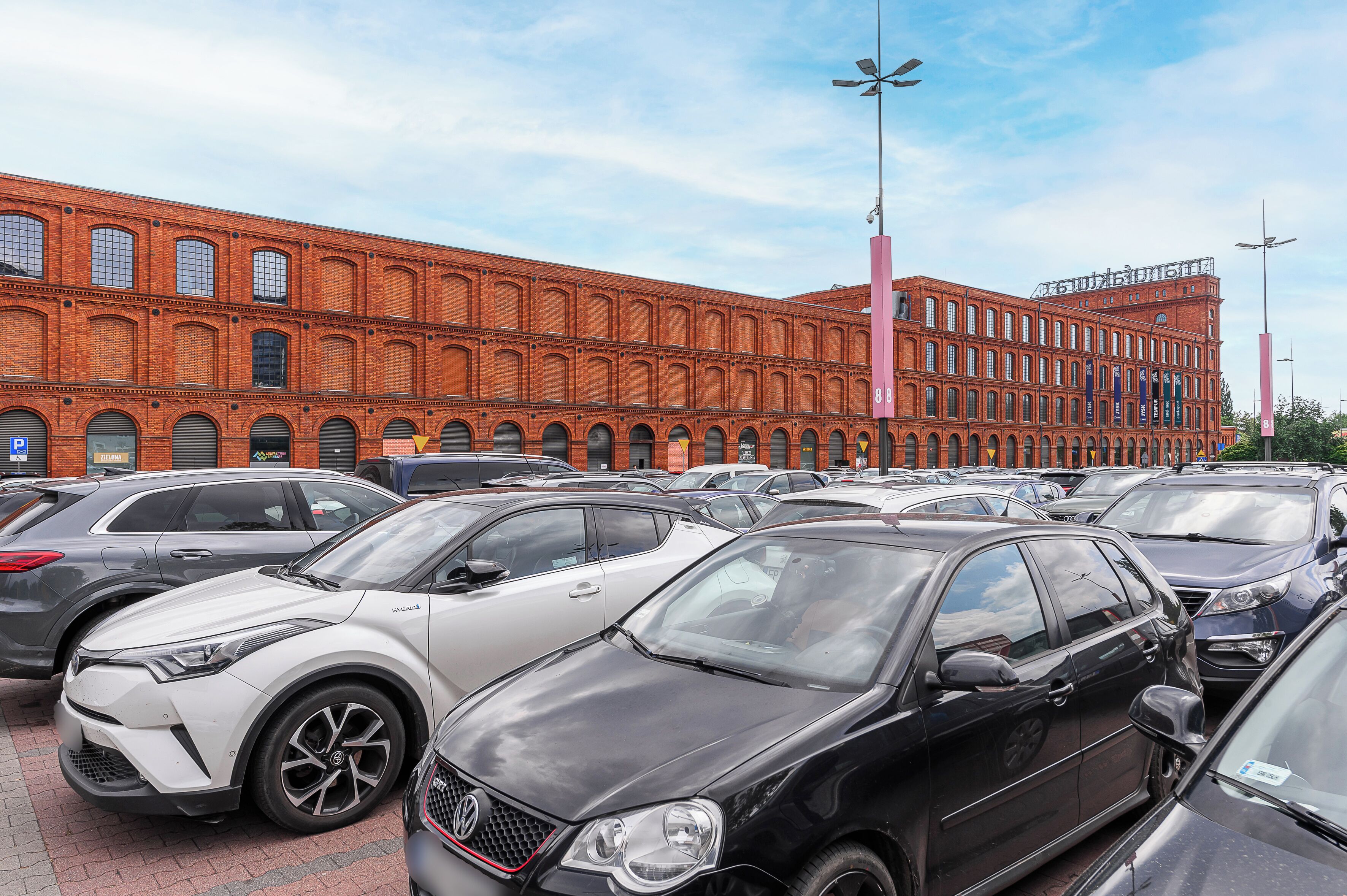 A parking lot with multiple cars and a large brick building in the background.