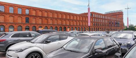 A parking lot with multiple cars and a large brick building in the background.
