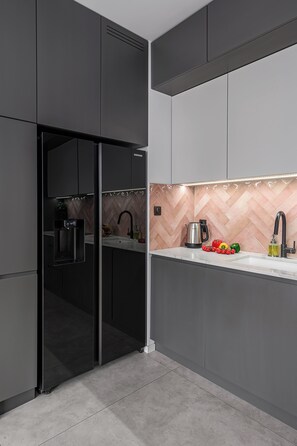 A modern kitchen with a built-in refrigerator, a herringbone-patterned backsplash, and a stainless steel kettle. - Lumina Apart nearManufartura and Parking (Łódź)