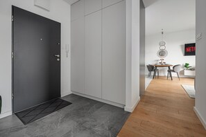 A modern interior with a black door, grey cabinets, a wooden dining table, and a TV displaying 'NETFLIX'. - Lumina Apart nearManufartura and Parking (Łódź)