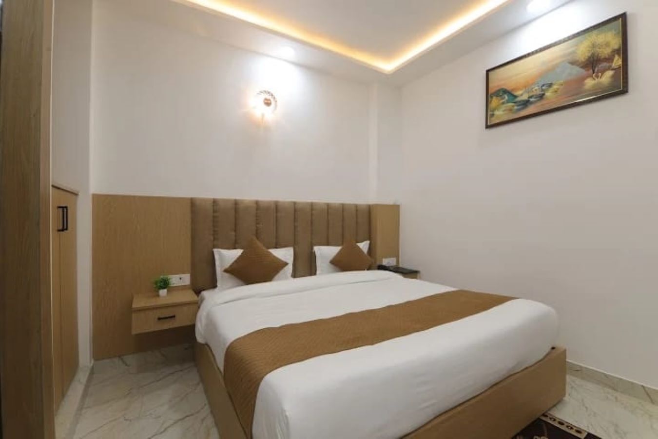 Une chambre d’hôtel avec un grand lit, une table de chevet, une lampe fixée au mur et un tableau.
