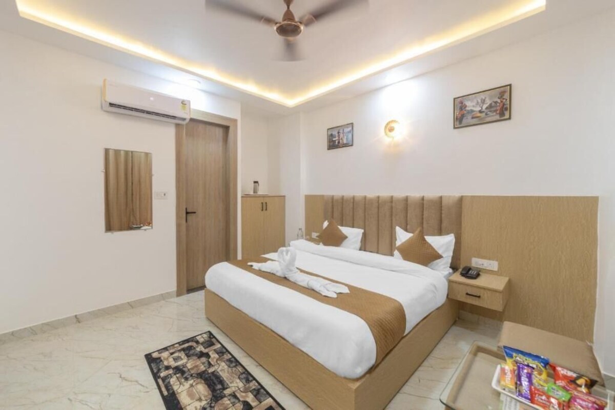 A hotel room with a large bed, bedside tables, an air conditioning unit, a ceiling fan, and a small table with snacks.