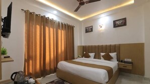 Habitación de hotel con cama, mesita de noche, ventilador de techo y televisor montado en la pared.