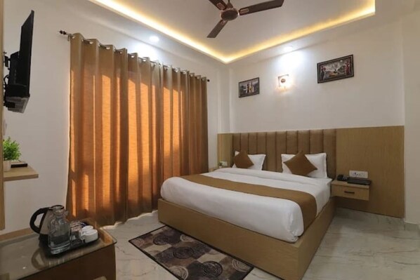 A hotel room with a bed, nightstand, ceiling fan, and wall-mounted TV. - HOTEL GANGA STONE (Haridwar)