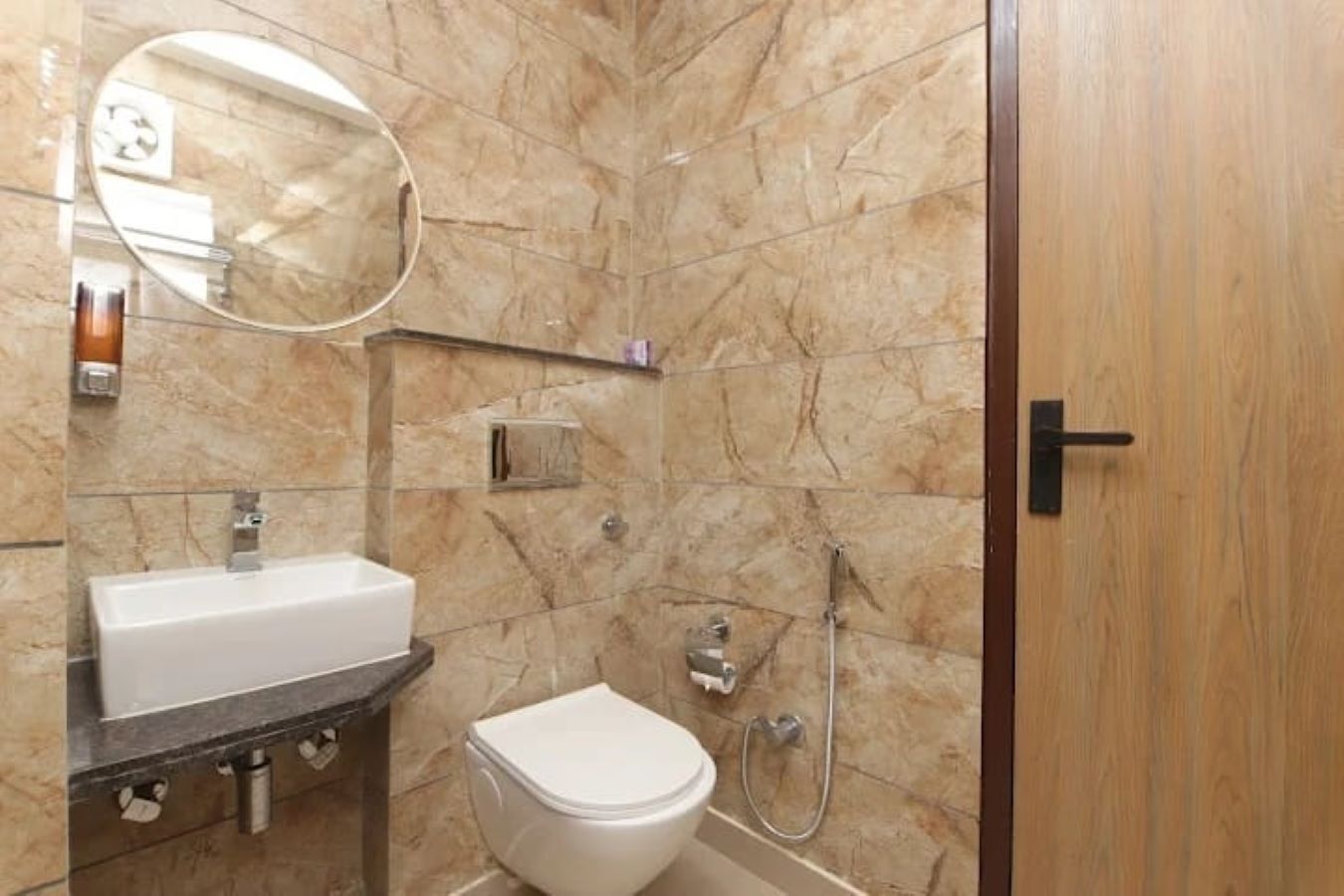 A bathroom with a marble wall, a sink, a toilet, and a shower.