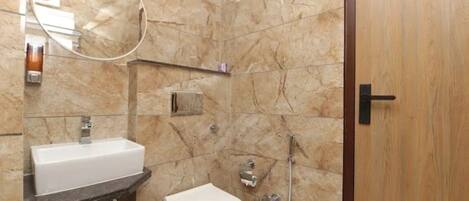 A bathroom with a marble wall, a sink, a toilet, and a shower.