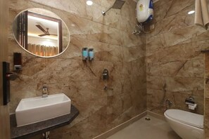 A bathroom with a marble wall, a sink, a toilet, a shower, and a ceiling fan. - HOTEL GANGA STONE (Haridwar)