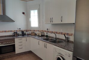 A kitchen with white cabinets, a stainless steel range, a washing machine, and a window. - Penthouse in Candelaria. Large terrace overlooking the cathedral (Cádiz)