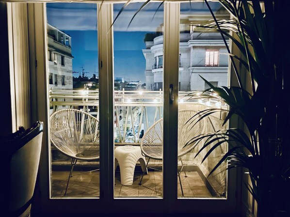 Ein Zimmer mit Glastür und Zugang zu einem Balkon, Korbstühle und einem Blumentopf.