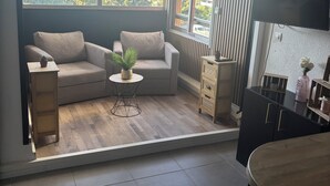Ein modernes Wohnzimmer mit einer Couch, einem kleinen runden Tisch mit Pflanze, einem Fernseher und einem Essbereich mit Tisch und Stühlen.
