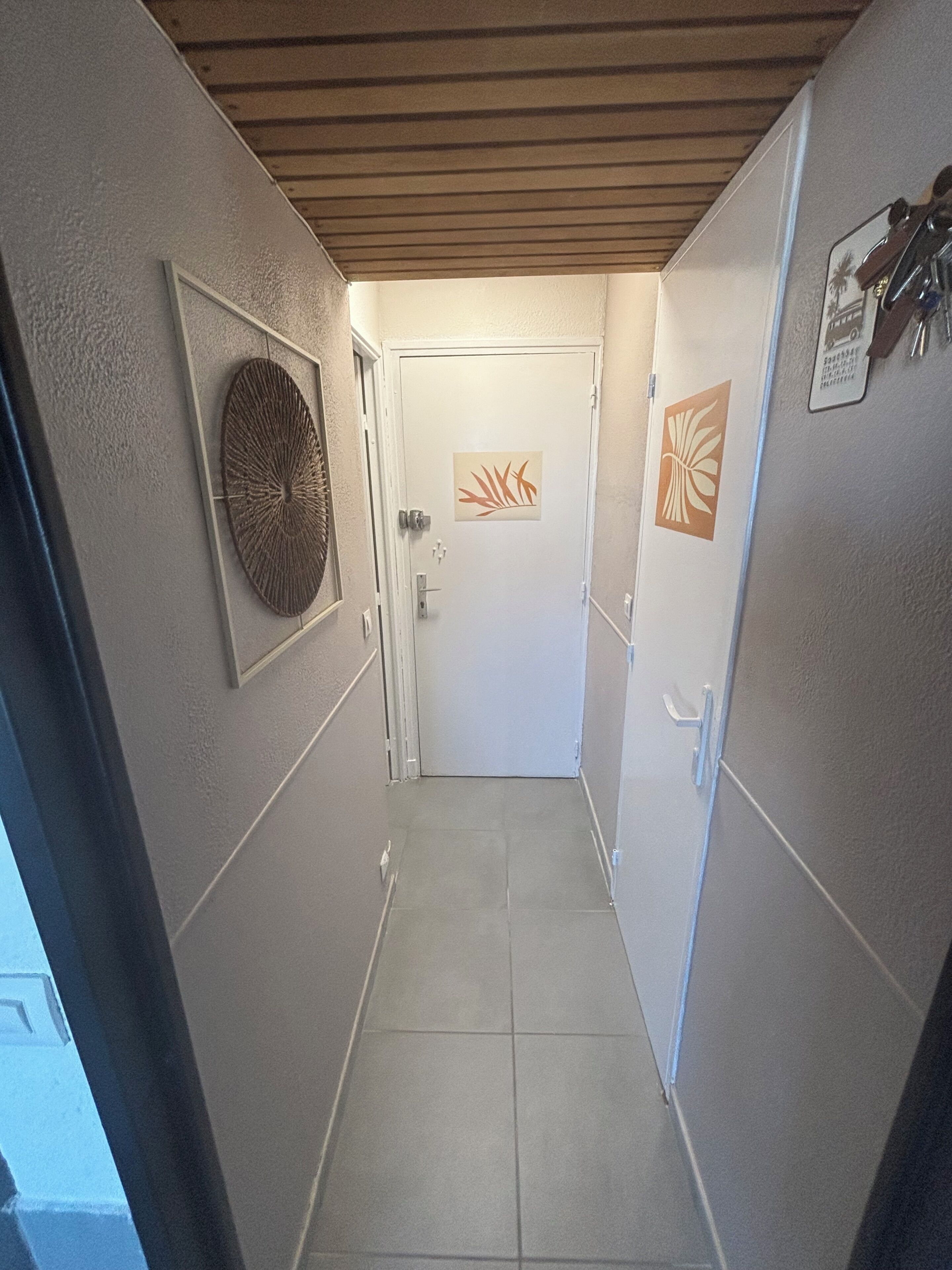 A narrow hallway with a wooden ceiling, a door with a leaf pattern, and a wall-mounted decorative item.