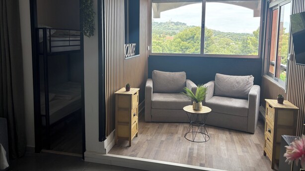 Ein Zimmer mit Etagenbett, einer Schlafcouch, einem kleinen Tisch und Blick auf Grünflächen.