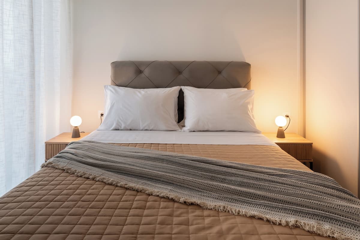 Una cama bien hecha con cubrecama acolchado, dos lámparas de noche y cabecera.