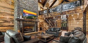 Ein Blockhaus-Interieur mit Kamin, Ledersofas, einem Essbereich und einer Treppe.