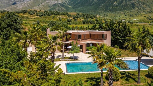 Une maison moderne avec une piscine, entourée d’une végétation luxuriante et de montagnes.